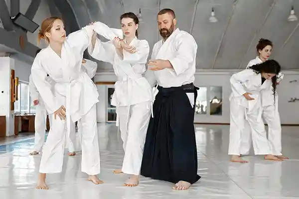 Two women practice Aikido defense position with male instructor helping