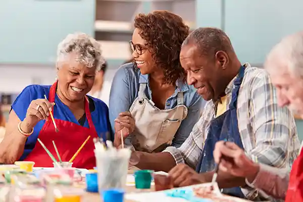 Senior adult students at table painting in class laughing with joy