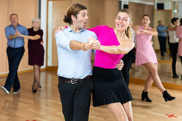 Image depicts young smiling girl dancing jive with her partner in Latin dance class