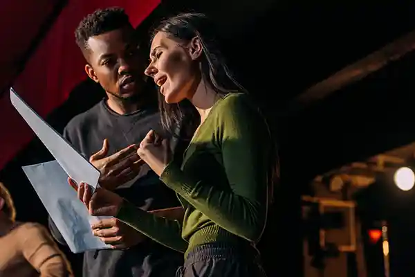 Male and female actors on a stage practicing from a script