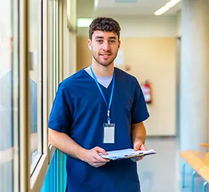Image depicts a confident male CNA reviewing patient files in a modern medical facility
