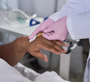 Image depicts close up of nurse placing IV into hand of patient in hospital