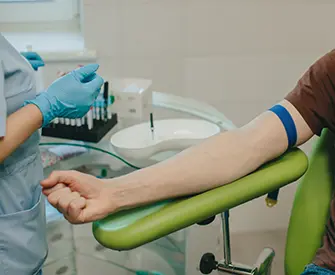 A phlebotomist in gloves prepares to collect blood in clinic from patient’s arm