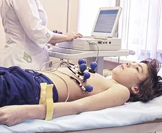 Image shows close up photo of EKG Tech performing ECG test on preteen boy