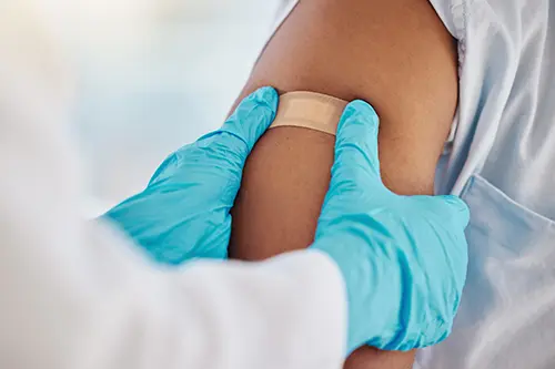 Doctor Applying Bandage to Patients Arm After Vaccine