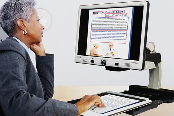 Woman sitting at a desk using a CCTV Desktop Magnifier.