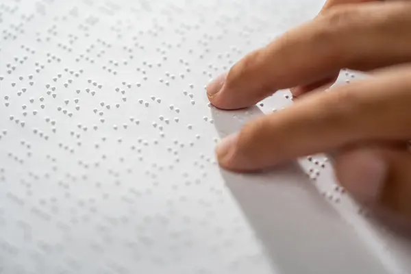 Hand of a blind person reading some braille text on page paper to learn.