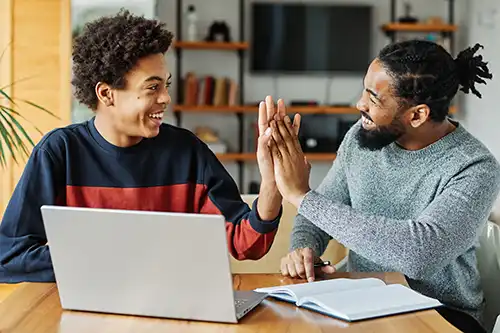Father and son doing homework with laptop at home giving high five