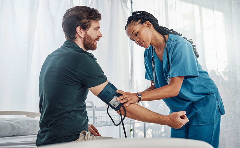A pair of blue, surgical-gloved hands putting a bandaid on a patient's upper arm.