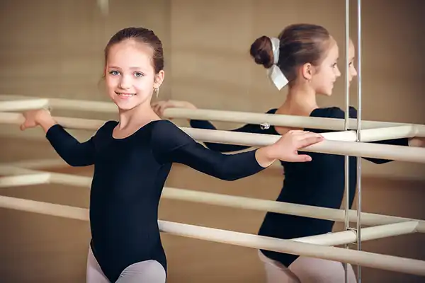Young girl in ballet suit standing at a dance class bar