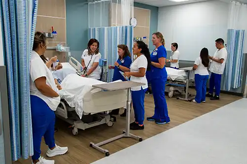 image depicts Simulation center station with students discussing patient