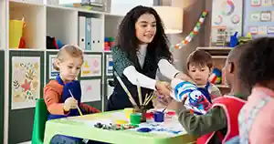 image depicts a young teacher working on a painting project with 3 young students